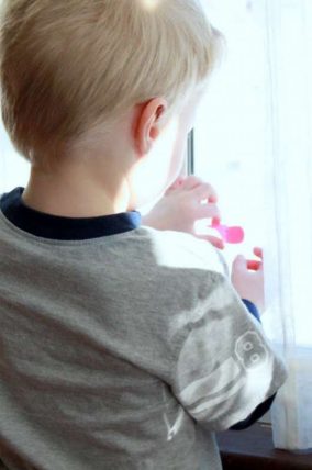 Child reaching up to place paper hearts on a window