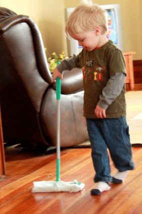 Toddler pushing a floor sweeper across a living room