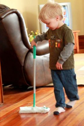 Toddler pushing a floor sweeper across a living room