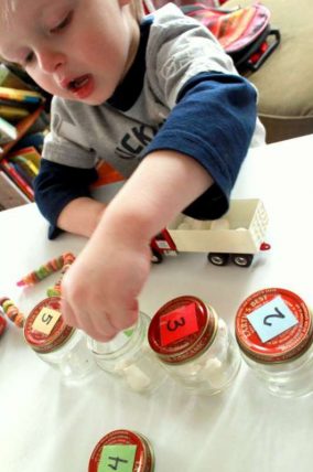 Child loading a toy truck beside numbered jars standing in for grain bins