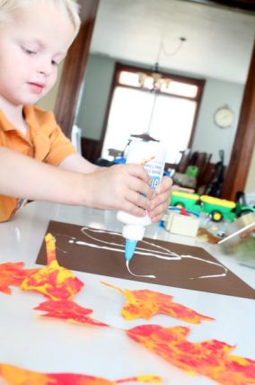 Child painting fall leaves in red and orange with bubble wrap prints