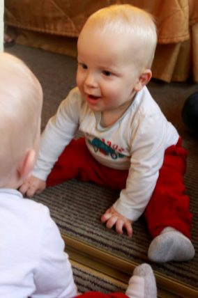 Two babies sitting face to face on a rug