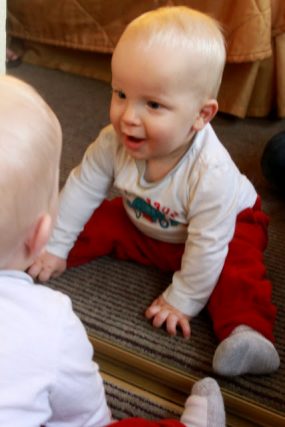 Two babies sitting face to face on a rug