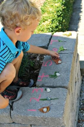 Child arranging leaves and acorns beside chalk numbers on a stone wall