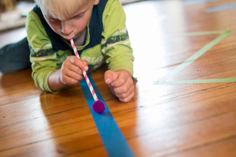 Work on breath control as you blow pom poms along lines of colored tape