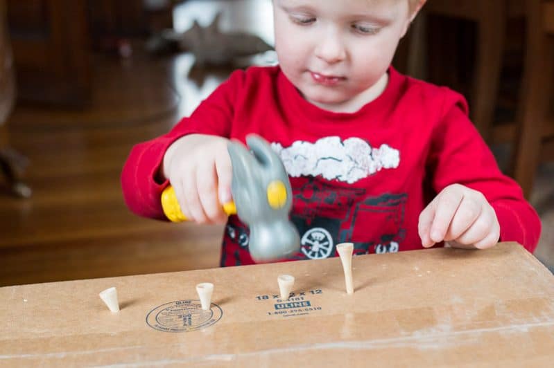 Work on fine motor skills with this super simple no prep hammering activity for toddlers using a cardboard box, golf tees, and toy hammer.