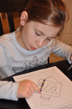 Child placing star stickers along the lines of a traced dreidel on a Hanukkah worksheet