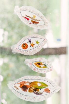 Leaf-shaped suncatchers made with pressed leaves and petals hanging in a window