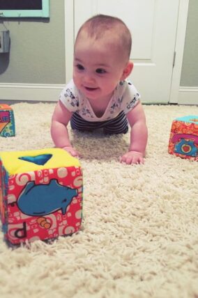 Baby crawling on carpet toward soft fabric blocks
