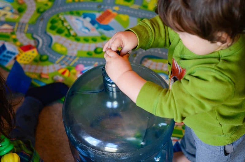 A simple gross motor activity that involves lifting and heavy work. A young toddler puts a toy into a large jug.