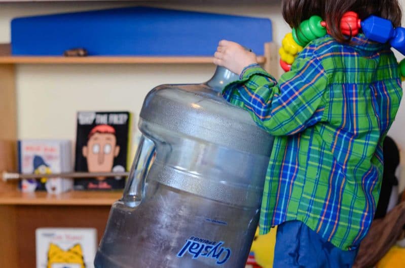 A simple gross motor activity that involves lifting and heavy work. A child carries the large jug around, looking for the next toy to put inside it.