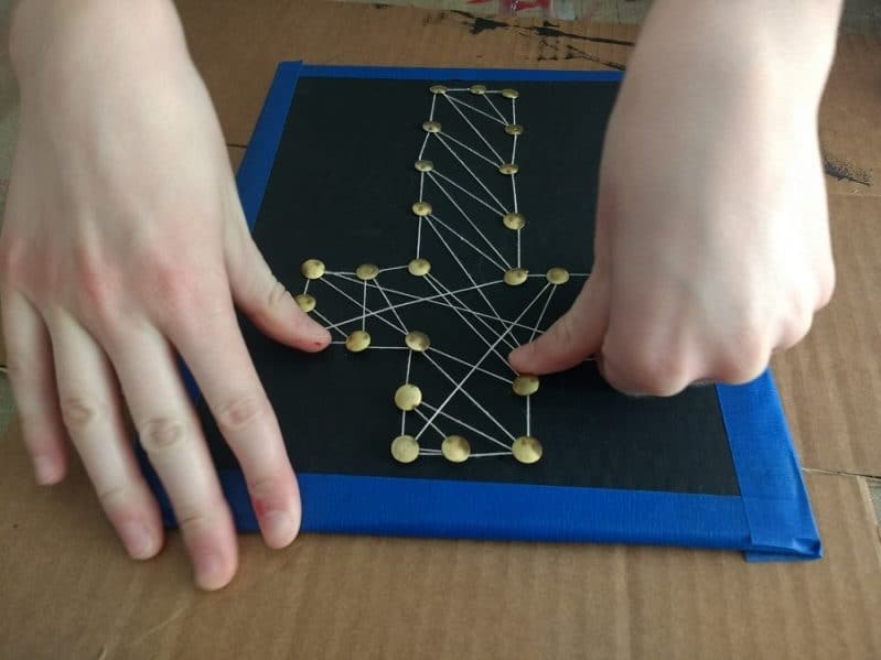 push down the tacks into the cardboard string art to hold the string in place