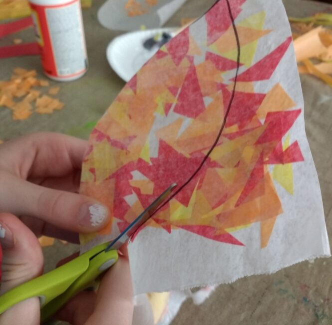 Cutting out the tissue paper leaf for suncatcher craft.