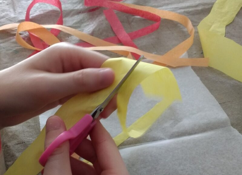 Cutting up tissue paper for leaf suncatcher craft for kids.