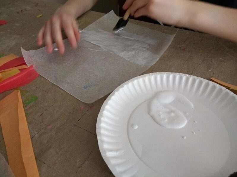 Painting glue on wax paper for leaf suncatcher craft for kids.