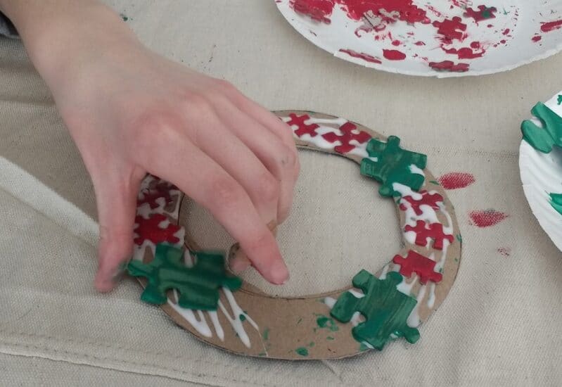 Gluing puzzle pieces on to cardboard for Christmas wreath