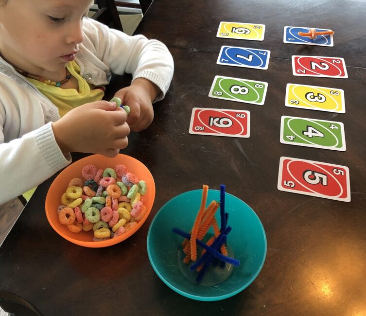 Threading Fruit Loops onto pipe cleaners. Use the Uno Card to decide how many Fruit Loops to thread!