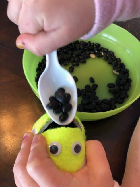 pouring a spoonful of beans into the tennis ball also builds hand-eye coordination and control.