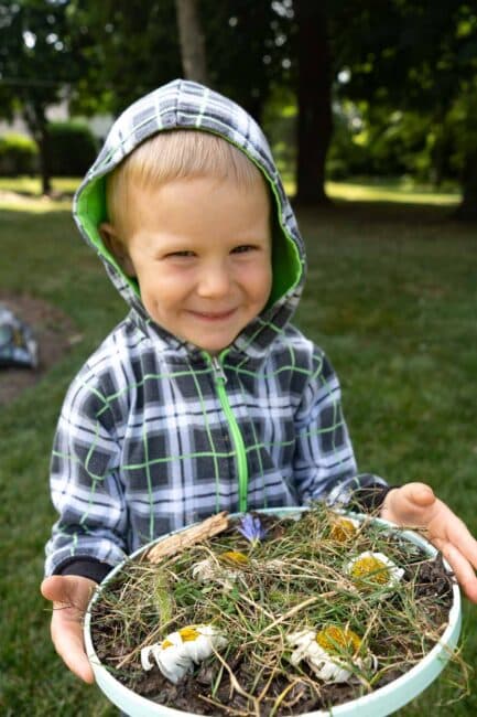Cooking pretend play pizza out of mud and nature items is a great creative and sensory activity to try outdoors with young kids this summer!