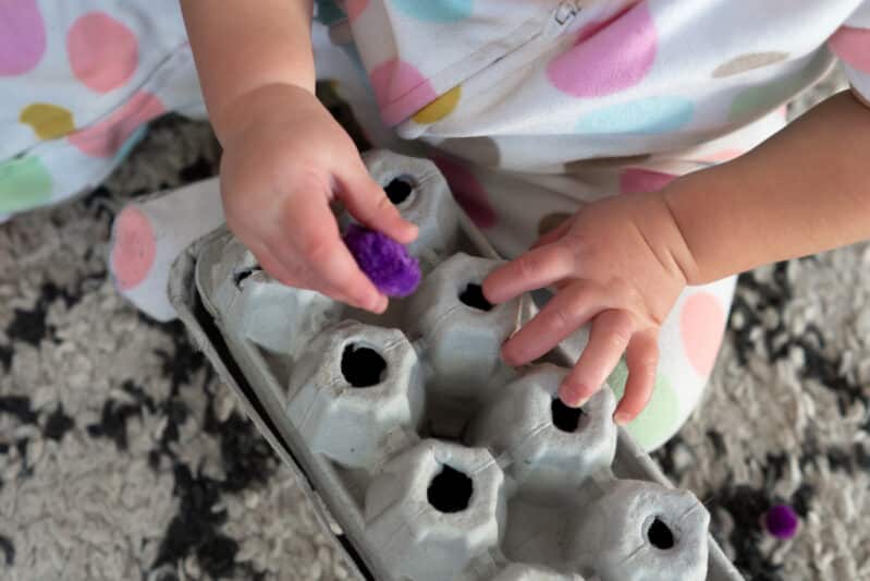 Work on fine motor skills with this easy to make fine motor push activity for toddlers using an egg carton and pom poms. Bonus, you can take it with you when you need to keep your toddler still and quiet!
