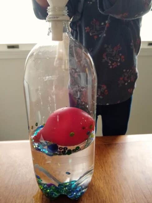 Grab a balloon, a sharpie, 2 litre bottle, blue food coloring, and water and create a little ocean sensory bottle with a swimming whale for lots of toddler and preschooler fun at home!