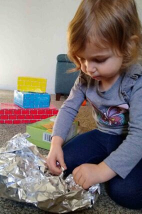 Toddler unwrapping objects hidden in aluminum foil