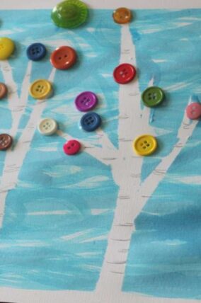 Colorful buttons attached to a painted birch tree on blue paper