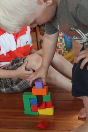 Child stacking colorful wooden blocks on a wood floor
