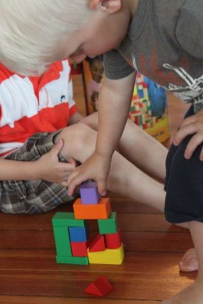 Child stacking colorful wooden blocks on a wood floor