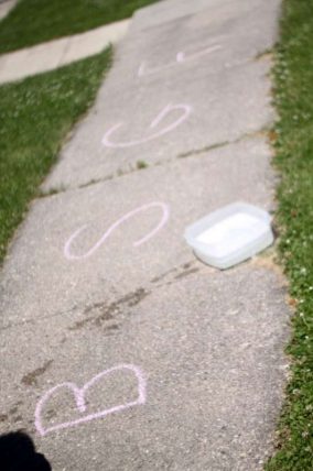 Chalk letters on a sidewalk beside a tub of water for washing toys