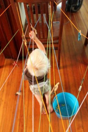 Child moving through a web of colored string strung across a room during a letter scavenger hunt