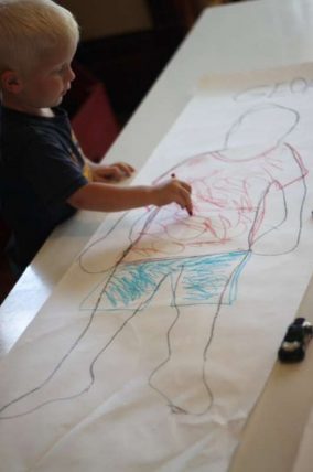 Child coloring in a life size body outline on a long sheet of paper