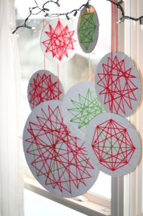 Yarn wrapped circle ornaments hanging in a window with string lights
