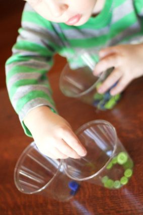 Child's hands sorting colored buttons into clear plastic bowls