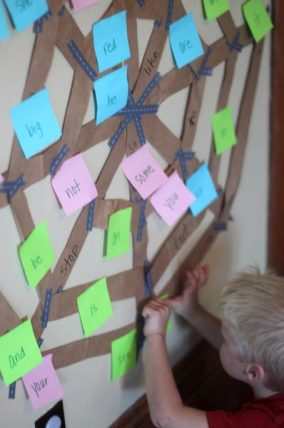 Child adding sticky notes with sight words to a masking tape web on a wall