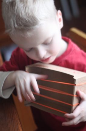 Child playing a homemade cardboard box instrument