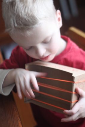 Child playing a homemade cardboard box instrument