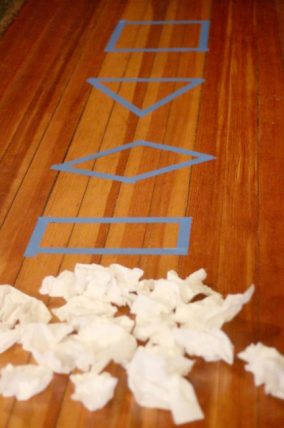 Blue tape shapes on a wood floor beside a pile of paper snowballs