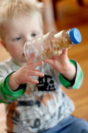 Toddler holding up a clear bottle filled with puffed cereal