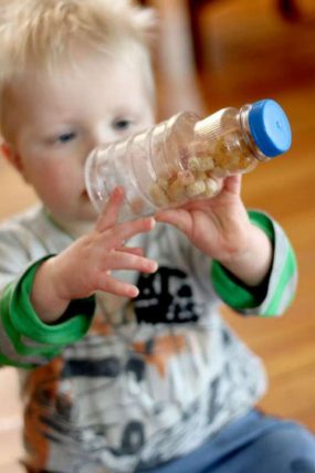 Toddler holding up a clear bottle filled with puffed cereal
