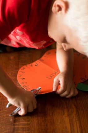 Child punching holes around an orange paper pumpkin marked with letters