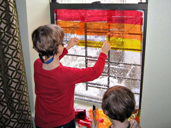 Sticking on the colors of cellophane onto the window for the rainbow window art.